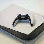 A PlayStation 5 with a DualSense controller laying on top.