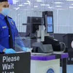 TSA agent standing next to facial recognition scanner